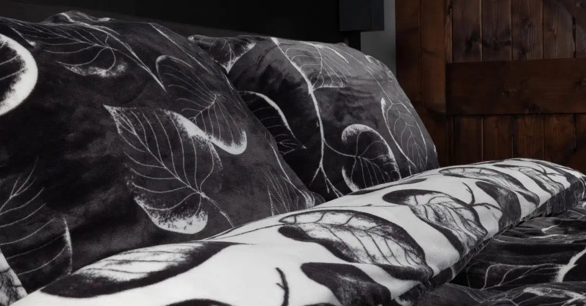 een luxe velvet dekbedovertrek met een bladerenpatroon ligt omgedraaid op een bed, vergezeld van twee bijpassende kussens in zachte kleuren. foto: dekbedovertrek bladeren andersom.