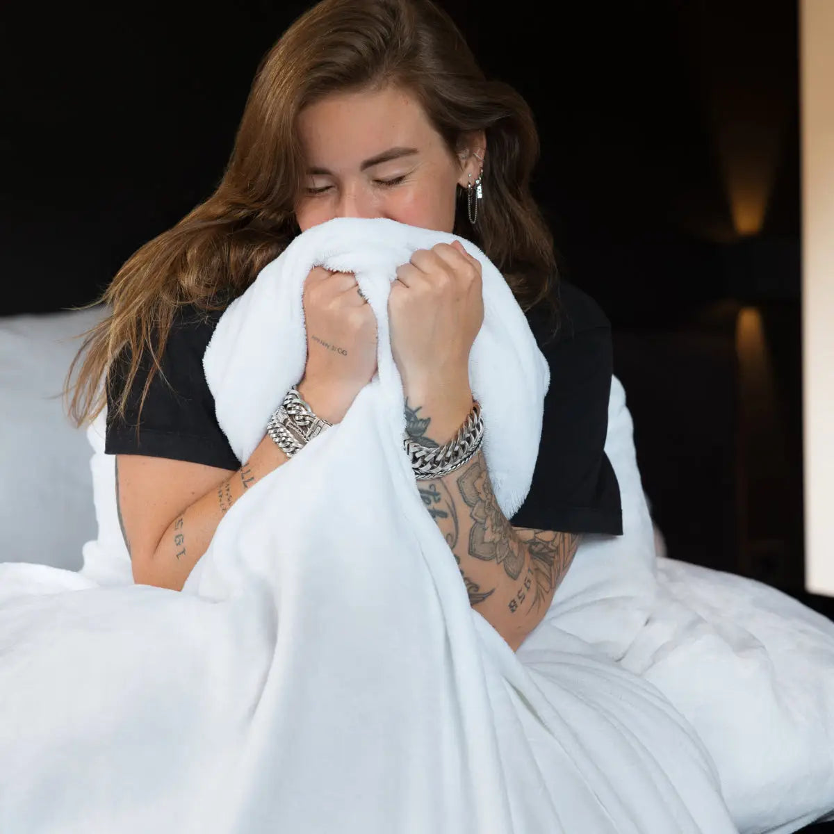 Een vrouw gewikkeld in een zacht, wit velvet dekbedovertrek. Het materiaal glanst subtiel in het licht, terwijl ze zich knus en warm voelt, omgeven door de luxe en zachtheid van de fluweelachtige stof. foto: dekbedovertrek wit met Lisa.