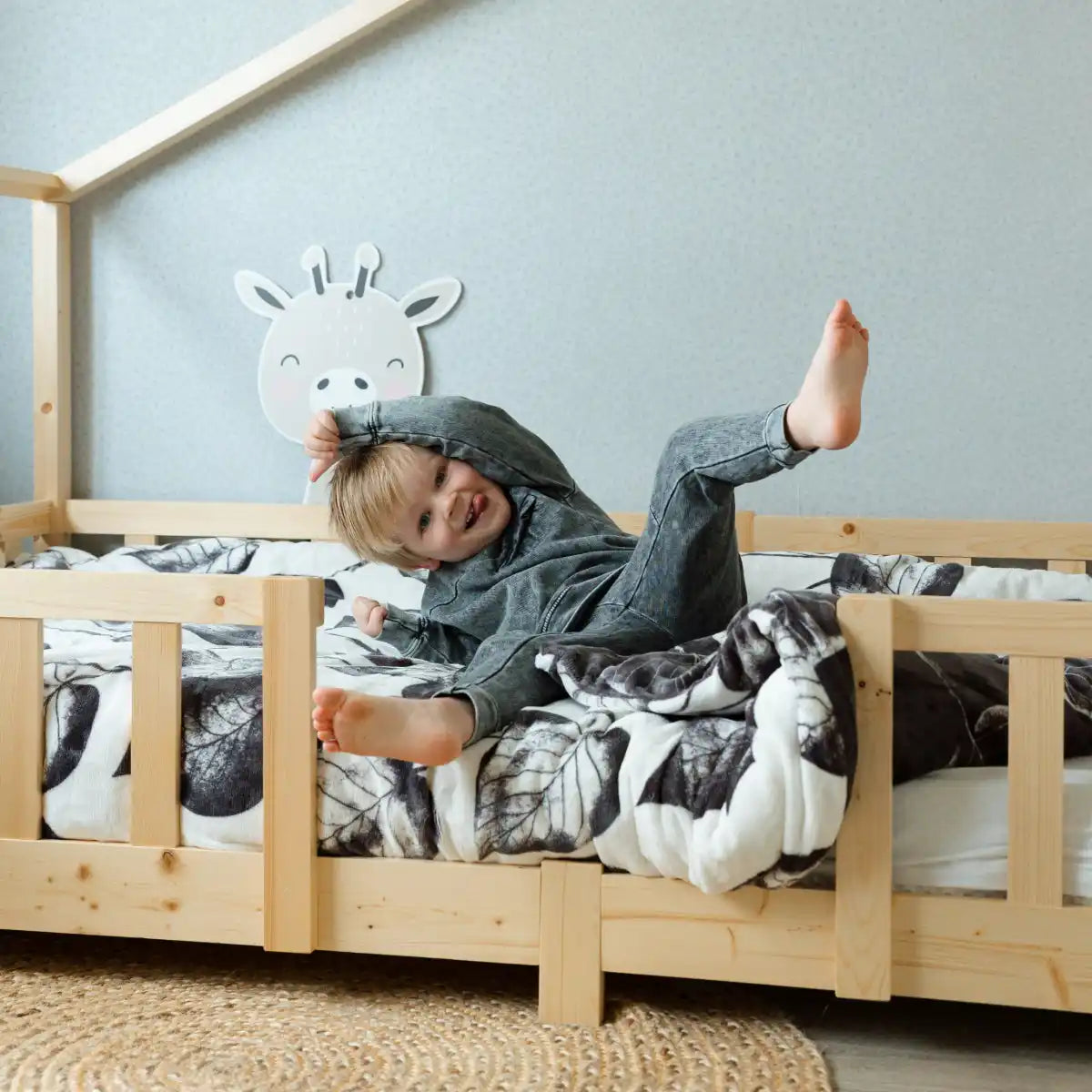 Een houten peuterbed met leuningen en bloemige beddengoed.