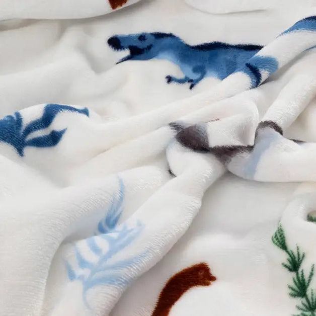 Alt-tekst: Een fluwelen dinosaurus kussen in zachte tinten ligt op een bed, omgeven door neutrale beddengoed. Het kussen heeft een aaibare textuur, met fijne details, en voegt een speelse touch toe aan de rustige slaapkamer. foto: kussen dino.