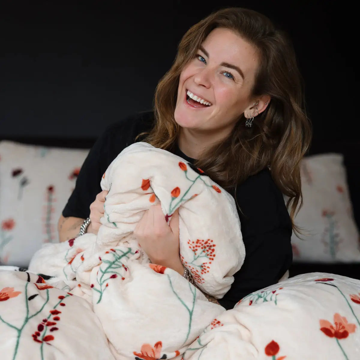 Een vrouw zit ontspannen met een velvet tweepersoons dekbedovertrek om haar heen gedrapeerd. Het dekbedovertrek heeft een kleurrijk patroon van levensechte klaprozen en straalt luxe uit. foto: dekbedovertrek klaproos met Lisa.
