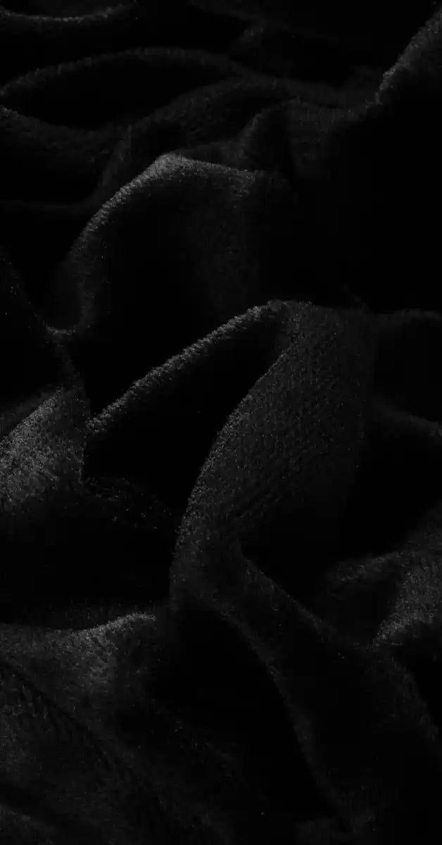 Close-up van zwart velvet stof van een kussen, met een fluweelachtige, zachte textuur. De stof heeft een luxe uitstraling en subtiele glans, wat het kussen een elegante en comfortabele uitstraling geeft. Foto: stof kussen zwart.
