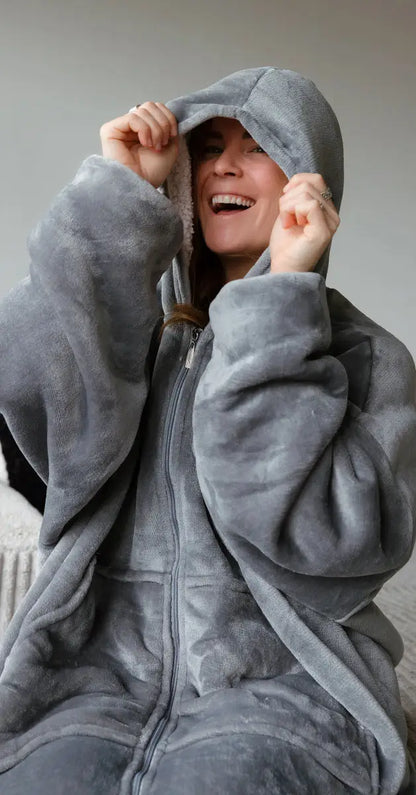 Een meisje zit op de bank en draagt een grijze hoodie met capuchon, die comfortabel gesloten is. Ze trekt de capuchon met haar handen over haar hoofd en lacht, wat haar blijdschap uitstraalt. De hoodie is gemaakt van ultrazacht velvet en is gevoerd met sherpa, ideaal om in te relaxen. De hoodie is verkrijgbaar in één maat die iedereen past.
foto: hoodie grijs met capuchon