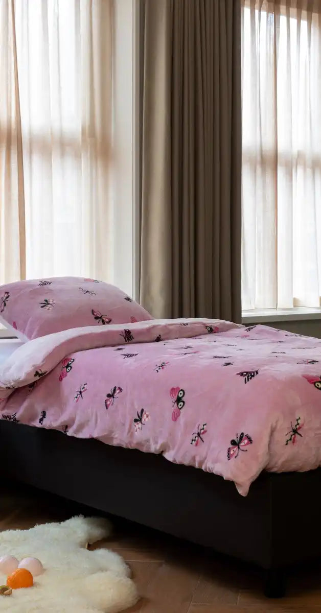 Roze beddengoed met vlinderpatronen op een bedframe.