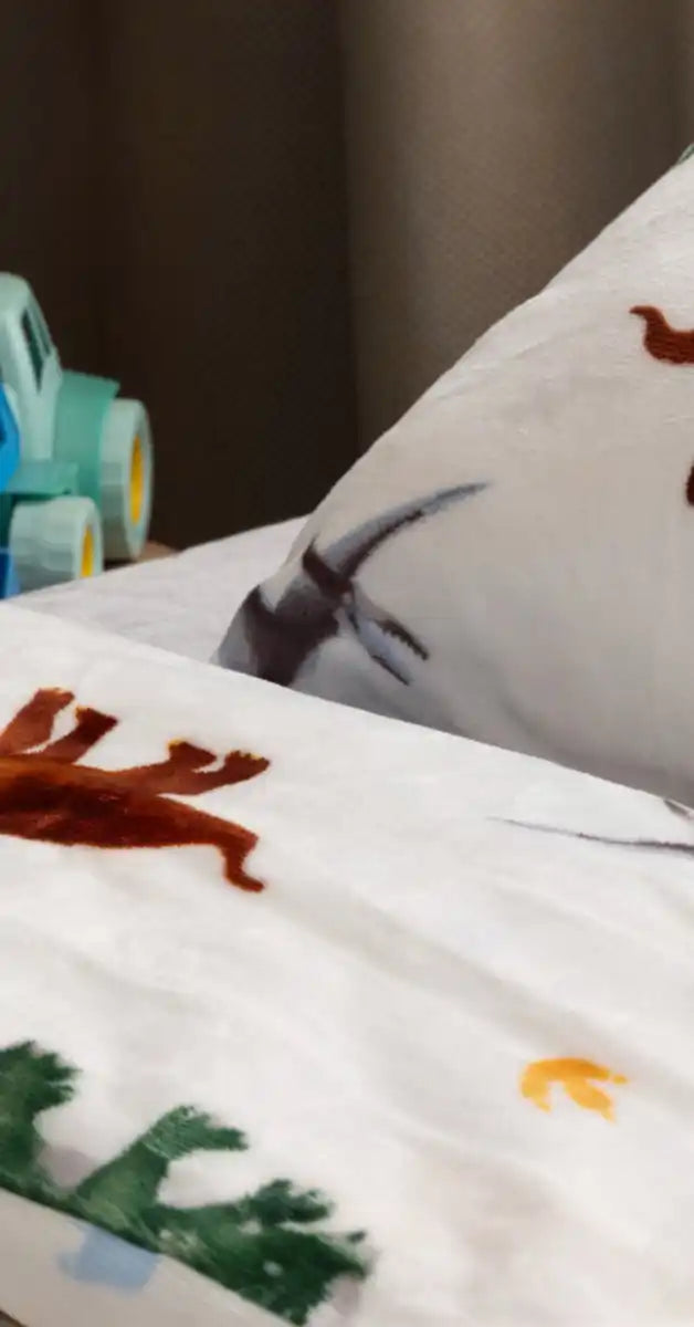 Witte beddengoed met kleurrijke dinosaurussenpatronen erop gedrukt.